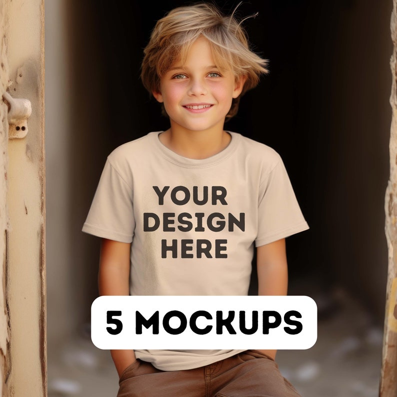 May include: A young person wearing a beige t-shirt with the text "YOUR DESIGN HERE" printed on the front. The t-shirt is a mockup for a design project. The image is labeled "5 MOCKUPS".