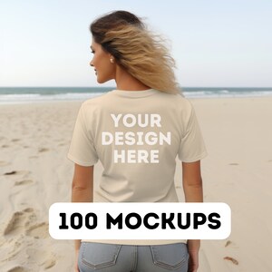 May include: A woman wearing a beige t-shirt with the text "YOUR DESIGN HERE" on the back. She is standing on a sandy beach with the ocean in the background.