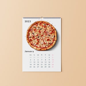 K&ouml;nnte beinhalten: Ein wei&szlig;er Kalender mit einer bunten Pizza oben und dem Monat Januar. Der Kalender ist f&uuml;r das Jahr 2023.
