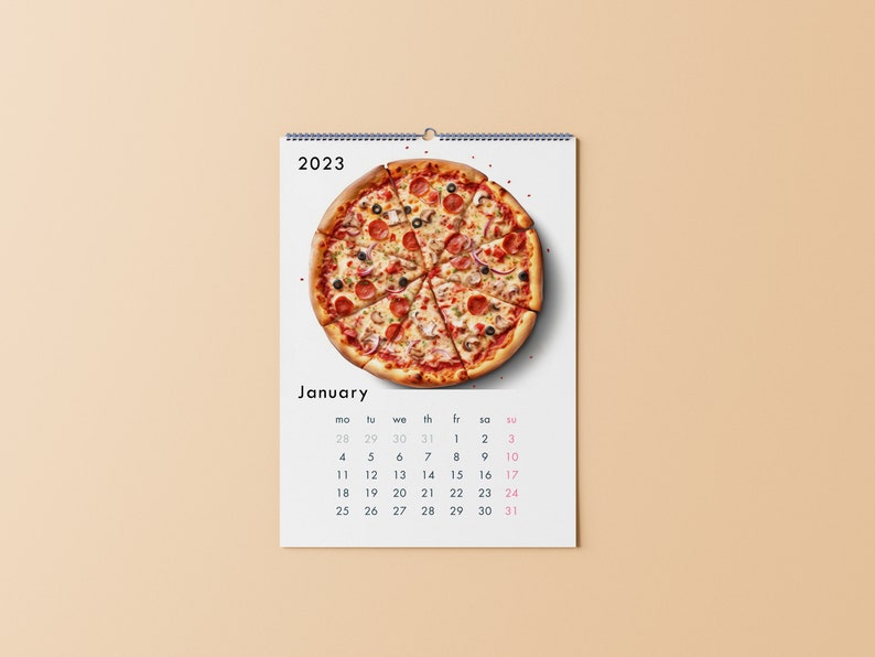 K&ouml;nnte beinhalten: Ein wei&szlig;er Kalender mit einer bunten Pizza oben und dem Monat Januar. Der Kalender ist f&uuml;r das Jahr 2023.