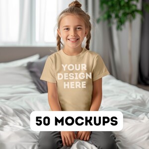 May include: A young person wearing a tan t-shirt with the text "YOUR DESIGN HERE" in white. The words "50 MOCKUPS" are displayed in a white rectangle at the bottom of the image. The person is sitting on a bed with white sheets.