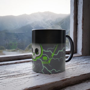May include: A black ceramic mug featuring a graphic of a white skull with a green heart-shaped nose, surrounded by bright green lightning bolts, a hockey stick, and a hockey puck. Steam rises from the top of the mug, which has a curved handle.