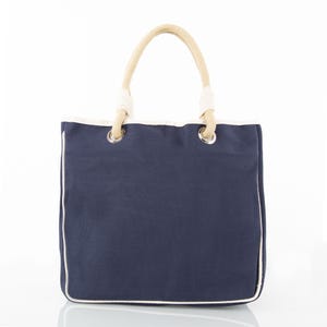 May include: Navy blue tote bag with a white trim and rope handles. The bag has a rectangular shape with a white border outlining the edges. The handles are made of thick, beige rope.
