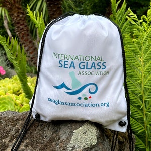May include: White drawstring bag with the logo "International Sea Glass Association" and the website "seaglassassociation.org" printed on it.