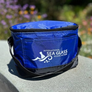 May include: A blue insulated cooler bag with a black zipper and handle. The bag has a white logo that says "International Sea Glass Association".