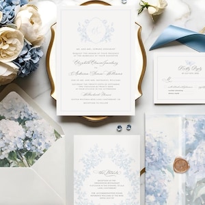 May include: A wedding stationery suite featuring cream and blue floral arrangements, invitation cards, and a blue satin ribbon. The invitation card includes the names "Elizabeth Claire Sanchez" and "Anderson Shane Williams". The stationery is arranged on a marble surface.