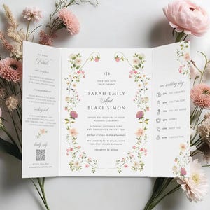 May include: A tri-fold wedding invitation with floral accents and the names Sarah Emily and Blake Simon. The invitation is surrounded by pink and beige flowers and greenery, creating a romantic aesthetic.