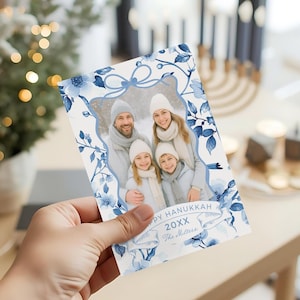 Op de afbeelding: Een Hanukkah-wenskaart met een familiefoto, omlijst door blauwe bloemmotieven. De kaart toont de tekst "Happy Hanukkah 20XX The Millers" op een banner. Het ontwerp is overwegend blauw en wit.