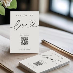 Peut inclure: Cartes crème avec l'inscription "CAPTURE THE love" en écriture cursive, un code QR et le texte "SCAN TO SHARE YOUR PHOTOS". Un vase de fleurs blanches et des stylos dorés sont sur la table en bois. La date "JUNE 12, 20XX" est également imprimée.