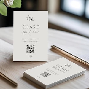 Puede incluir: Tarjetas de color crema con el texto "SHARE the love" y un código QR, con un jarrón de flores blancas. Bolígrafos dorados están sobre la mesa. Las tarjetas son para compartir fotos. El texto también dice "SCAN THE QR CODE TO SHARE YOUR PHOTOS".