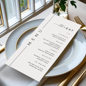 May include: A menu card with the words "MENU" and "let's EAT" printed in black. The menu lists starters, mains, sides, dessert, and drinks. The card is on a white plate with a gold rim, next to gold silverware.