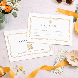 Puede incluir: Juego de invitaciones de boda con dos tarjetas blancas con bordes dorados. Las tarjetas dicen "KINDLY REPLY" y "KINDI by jury". La imagen también muestra un código QR, anillos de oro en una concha, gafas de sol y una cinta amarilla.
