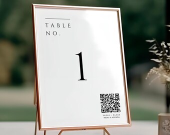 May include: A rose gold metal table number sign with the text "TABLE NO. 1" in black. A QR code and the text "SARAH BLAKE MENU & AGENDA" are also visible. The sign is displayed on a table with flowers in the background.