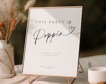 Może przedstawiać: Biały znak z pozłacanym ramieniem na złotym stojaku. Na znaku widnieje napis "This party is poppin'" z narysowanym sercem obok słowa "poppin". Pod tekstem widnieje napis "Please help yourself" oraz "Sarah & Blake 10.12.XX".