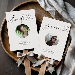 Puede incluir: Dos abanicos de despedida de soltera marfil con las palabras "bride" y "groom" en escritura elegante. Cada abanico presenta una foto circular y el texto "June 10, 20xx, Elianna's Bridal Shower." Los abanicos están adornados con lazos beige.