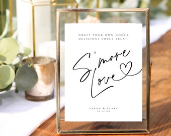 May include: A gold-framed sign with a white background and black text that reads "Craft your own gooey delicious sweet treat! S'more Love" with a heart symbol. The sign also includes the names "Sarah & Blake" and the date "10.12.XX".