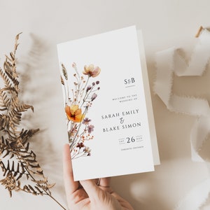 May include: A wedding invitation featuring a watercolour illustration of wildflowers in shades of orange, yellow, and purple. The text reads "S&B Welcome to the Wedding of Sarah Emily & Blake Simon Sat 26 Aug Toronto, Ontario."