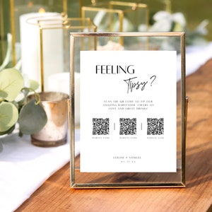 May include: A white sign in a gold frame with the text "Feeling Tipsy?" and three QR codes. The text below the QR codes says "Website Name" and "Louise + Samuel" with the date "03.31.XX".