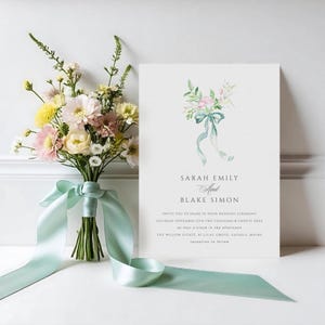 May include: A wedding invitation with a watercolor illustration of a bouquet of flowers with a blue ribbon. The invitation reads "Sarah Emily and Blake Simon" and includes the date, time, and location of the wedding ceremony.