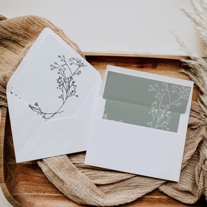 May include: Two white envelopes with a floral design. The envelope on the left has a black floral design and the envelope on the right has a grey floral design.