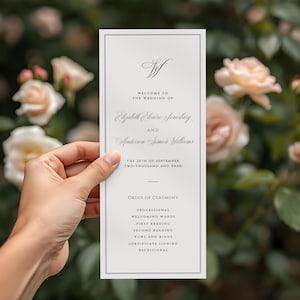May include: A wedding program with a gray border, held in front of a blurred floral background. The program features elegant script with the names Elizabeth Elouise Jonesbury and Anderson Simon Williams, and the date.