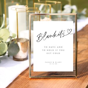 May include: A gold-framed sign with the text "Blankets" in cursive with a heart symbol. The sign also says "To have and to hold if you get cold" and "Sarah & Blake 10.12.XX".