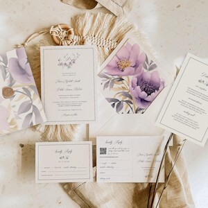 May include: A wedding invitation suite with a watercolor floral design in shades of purple and gray. The invitation features the couple's names and wedding date. The RSVP card includes a QR code and a space for guests to indicate their attendance.