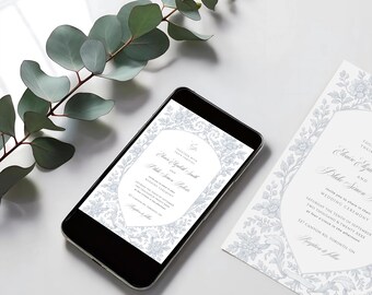 Op de afbeelding: Een smartphone toont een trouwuitnodiging met een bloemmotief in lichtblauw en wit. Een bijpassende uitnodigingskaart ligt naast de telefoon. Eucalyptustakken zijn op de achtergrond. De uitnodiging bevat de namen van het paar en huwelijksdetails.