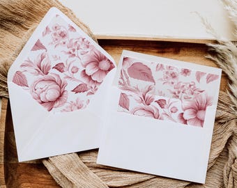 May include: Two white envelopes with a floral pattern in shades of pink. The envelopes are on a brown surface.