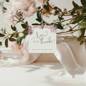 May include: A white wedding favor tag with purple flowers and the text "love and thanks Sarah & Blake".
