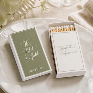May include: Two rectangular matchboxes with white and sage green covers. One box is closed, displaying the text The Perfect Match and JUNE 20, 20XX. The other box is open, revealing wooden matches and displaying the text Elizabeth & Anderson.