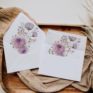May include: Two white envelopes with floral designs. The envelope on the left has a purple and pink floral design. The envelope on the right has a purple floral design.