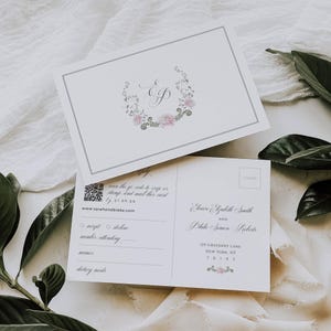 May include: Two white wedding invitation postcards. The front of the top card has a floral wreath with the letters "E" and "P". The bottom card has a QR code, reply options, and address details. The text includes "Sarahandblake.com".