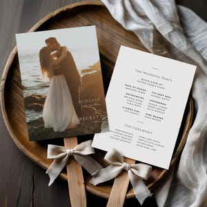 Könnte beinhalten: Hochzeitspapeterie-Set mit einem Foto eines sich küssenden Paares am Strand und einem Hochzeitsablauf. Das Programm listet die Hochzeitsgesellschaft und Zeremoniedetails auf und wird durch Holzfächergriffe und beige Schleifen akzentuiert.