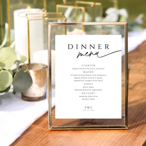 Puede incluir: Un menú de boda enmarcado en oro con fondo blanco y texto negro. El menú enumera las opciones de cena para una recepción de boda, incluyendo entrante, platos principales, acompañamientos, postre y los nombres de la pareja y la fecha de la boda.