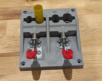 May include: A gray 3D-printed tool with two compartments, each secured by a metal latch with a red handle. A yellow cylinder is in one compartment. The tool is labeled "HARRIS 3D" and has markings for sizes 410, 28, and 12.