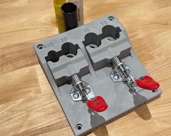 May include: A gray 3D printed reloading tool with two clamps. The clamps have red handles and are labeled with the numbers 12, 16, 20, and 410.