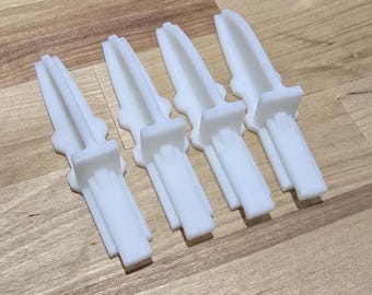 May include: Four white plastic dagger-shaped objects are arranged on a wooden surface. Each dagger has a rectangular handle and a blade with a pointed tip. The objects appear to be 3D-printed.