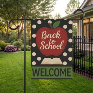 Może przedstawiać: Dekoracyjna flaga ogrodowa z czarnym tłem i białymi kropkami. Duże czerwone jabłko z napisem "Back to School" jest umieszczone na środku. Poniżej znajduje się otwarta książka i słowo "WELCOME". Flaga jest na czarnym stojaku.