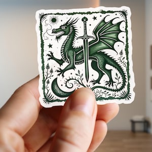 Puede incluir: Un dragón verde con las alas extendidas, sosteniendo una espada en sus garras. El dragón está rodeado por un borde decorativo de hojas y estrellas.