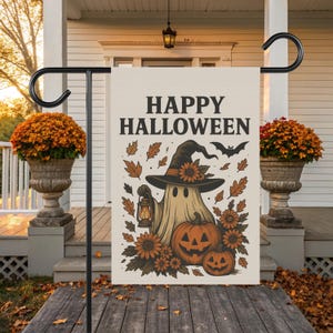 以下が含まれることがあります： 「HAPPY HALLOWEEN」の文字が黒で書かれたハロウィーンのガーデンフラッグ。魔女の帽子をかぶった幽霊がランタンを持ち、カボチャ、花、葉、コウモリが描かれています。フラッグは黒い金属製のスタンドに飾られています。