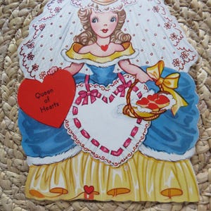 May include: Vintage Valentine's Day card featuring a cartoon queen in a blue dress with a yellow skirt. The card has a heart-shaped apron and a red heart with the text "Queen of Hearts". A basket of hearts is in her hand.