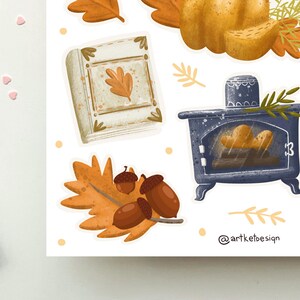 K&ouml;nnte beinhalten: Ein Set mit Herbst-Stickern, die ein Buch, einen Holzofen, Eicheln und Bl&auml;tter zeigen. Die Sticker sind auf wei&szlig;em Hintergrund mit einem hellbraunen Rand.
