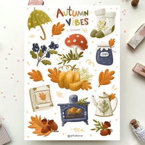K&ouml;nnte beinhalten: Ein Bogen Aufkleber mit Herbst-Motiv. Die Aufkleber zeigen Illustrationen von einem K&uuml;rbis, einem Pilz, einem Glas Marmelade, einem Buch, einem Kamin, einer Teekanne, einem Regenschirm, Socken und Bl&auml;ttern. Der Text "Autumn Vibes" und "Stickers" ist auf dem Bogen gedruckt.