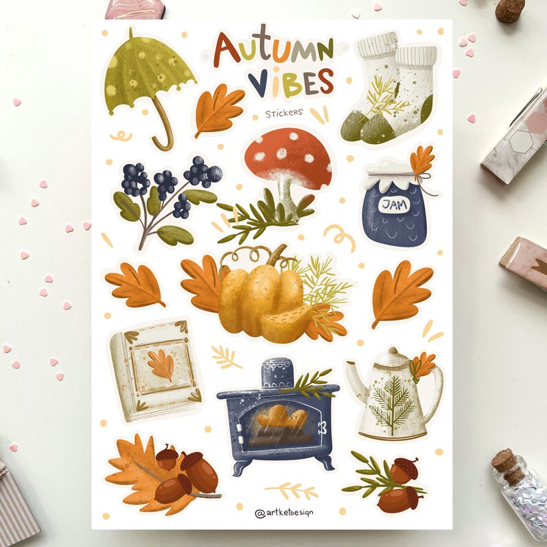 K&ouml;nnte beinhalten: Ein Bogen Aufkleber mit Herbst-Motiv. Die Aufkleber zeigen Illustrationen von einem K&uuml;rbis, einem Pilz, einem Glas Marmelade, einem Buch, einem Kamin, einer Teekanne, einem Regenschirm, Socken und Bl&auml;ttern. Der Text "Autumn Vibes" und "Stickers" ist auf dem Bogen gedruckt.