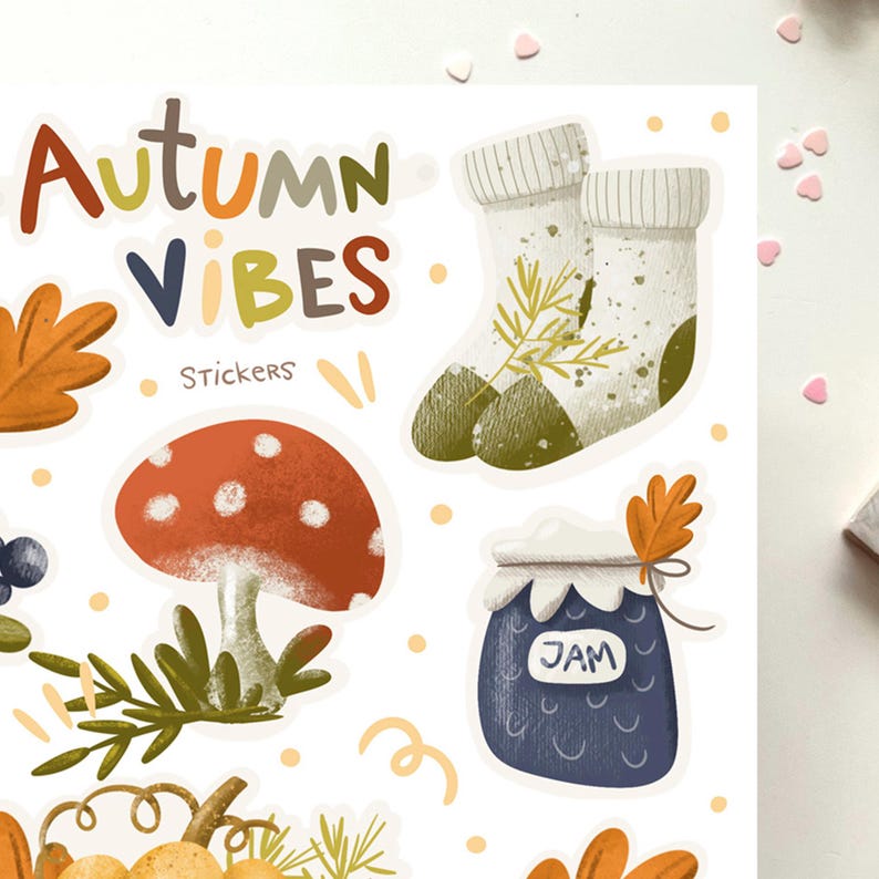 K&ouml;nnte beinhalten: Ein Set mit Herbst-Stickern, die einen Pilz, ein Glas Marmelade, ein Paar Socken und Bl&auml;tter zeigen. Die Sticker sind auf wei&szlig;em Hintergrund und im handgezeichneten Stil gehalten. Der Text "Autumn Vibes Stickers" befindet sich oben im Bild.