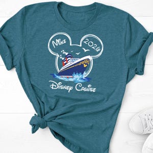 May include: Teal t-shirt featuring a Disney Cruise design. The graphic includes a cruise ship, the words "Disney Cruise", the name "Mike", and the year "2026" in a Mickey Mouse ear outline. The shirt is knotted at the waist.