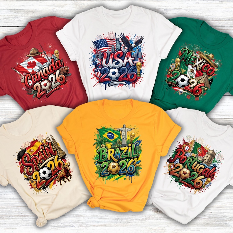 May include: A collection of short-sleeved t-shirts in various colors, each featuring a unique graphic design. The designs include country flags, soccer balls, and the year "2026". The shirts are in red, white, green, yellow, and beige.