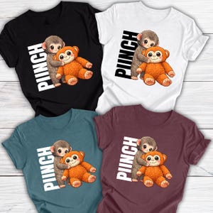 May include: Four t-shirts in black, white, teal, and burgundy. Each shirt features a cartoon illustration of a gray monkey hugging an orange teddy bear, with the word "PUNCH" in white, diagonally across the design. The shirts are short-sleeved.