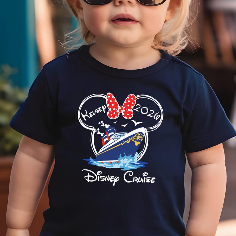 May include: Navy blue t-shirt featuring a Disney Cruise design. The design includes a cruise ship, the text "Disney Cruise", the name "Kelsey", the year "2020", and a red polka dot bow. The shirt is designed for children.